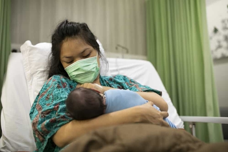 Mother holds newborn baby in hospital bed