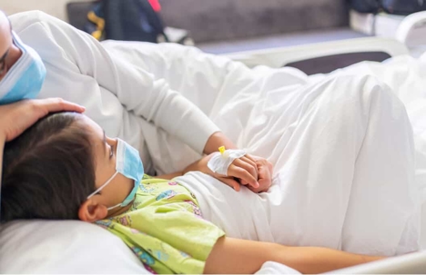 Child lays in hospital bed and mother lays with him for comfort