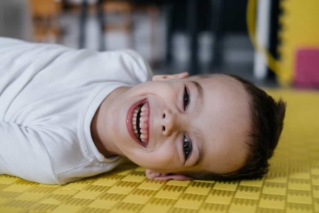 Young boy with cerebral palsy lays on a yellow cushioned floor mat designed for kids