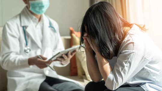 Upset patient holds her head in her hands in grief with a doctor next to her