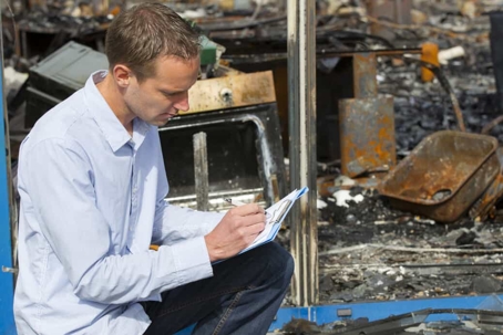 Young insurance adjuster looks over damage to a devastated home