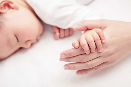 A baby sleeping and holding a parents hand