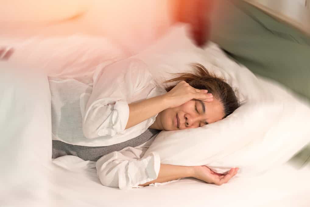 Woman lays in bed clutching her temple in pain